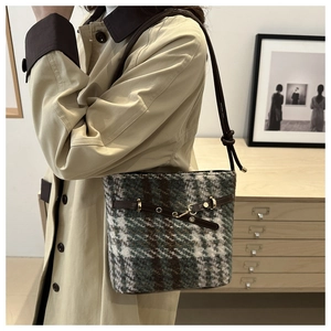 Detail of plaid bucket bag featuring leather strap and metal buckle on trench coat outfit