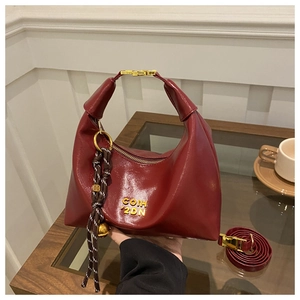 Close-up of wine red crescent bag with glossy finish, gold logo and woven charm