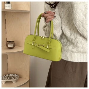 Lime green structured handbag with belt detail held by model against minimalist shelves