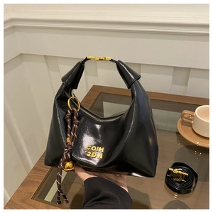 Detail of glossy black dumpling bag with gold logo, woven pendant and crossbody strap
