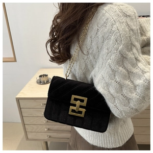 Detail of a black velvet crossbody bag with a gold rectangular buckle and chain strap