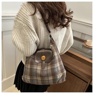 Detail of a brown plaid woolen crossbody bag with a golden circular metal clasp