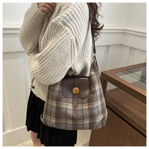 Detail of vintage plaid wool tote with brown leather flap and golden N-buckle on model