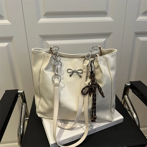 Minimalist cream white tote bag with silver bow and chain strap on a vintage chair