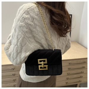 Detail of black velvet crossbody bag with golden chain and geometric buckle on model