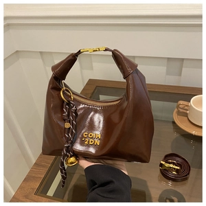 Detail of dark brown glossy leather dumpling bag with gold zipper and woven charm