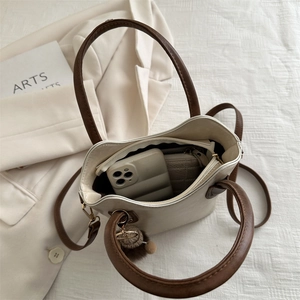 Retro cream white bucket bag with brown straps and pompom charm on a white fabric background
