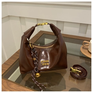 Close-up of crescent moon leather bag with gold buckle and woven charm on a glass surface