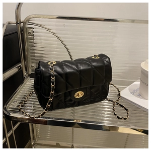 Detail of black quilted leather texture with gold turn-lock closure and chain strap