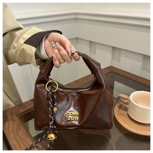 Close-up of brown glossy leather dumplings bag with gold logo and bell charm detail