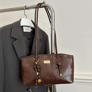 Dark brown faux leather tote bag with braided charm detail on a minimalist hanger