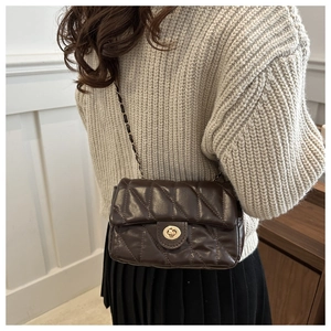 Sac bandoulière matelassé marron foncé avec chaîne dorée porté par un mannequin