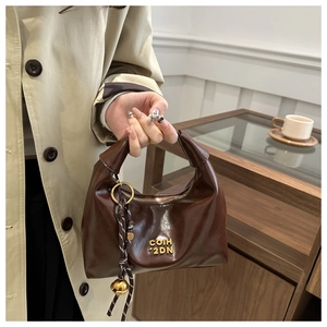 Detailed close-up of a brown oily leather dumpling bag with gold logo and bell charm