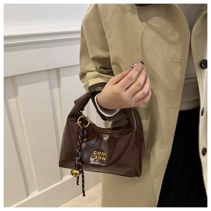 Close-up of a vintage glossy dark brown dumpling bag with golden logo and woven charm