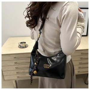 Detail of black glossy leather dumpling bag with gold COIH 2DN logo and bead pendant