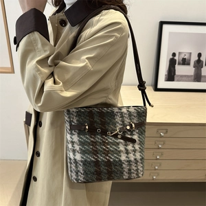 Retro plaid bucket bag with brown leather strap worn by a model in a minimalist room