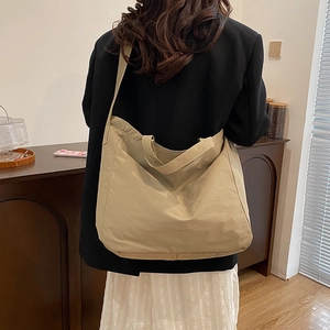 Khaki nylon tote bag with wide shoulder strap shown on a model in a cozy interior