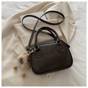 Detail der dunkelbraunen Ledertasche mit Lucky-Prägung und Schaf-Anhänger auf Blazer