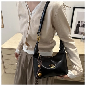 Detail of black crescent bag featuring golden logo and woven charm with metallic ball