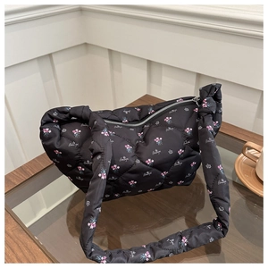 Detail of black quilted puffer bag with floral print and knot strap on a coffee table