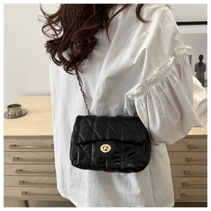 Detailed view of black quilted crossbody bag with golden clasp and chain strap on model