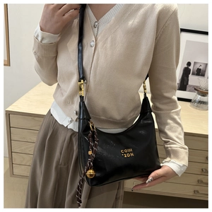 Detail of black crescent leather crossbody bag with gold logo and woven charm pendant