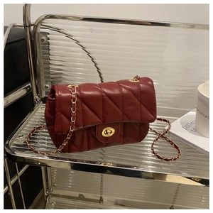 Détail d'un sac à chaîne matelassé rouge foncé avec fermoir doré sur étagère en métal