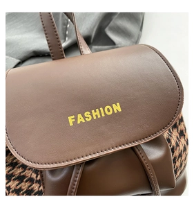 Detail of vintage brown leather backpack with yellow fashion text and houndstooth side panels