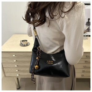 Close-up of black leather crescent bag with gold logo and woven tassel detail