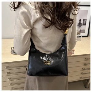 Detail of a black glossy crescent shoulder bag featuring a metallic logo and gold hardware