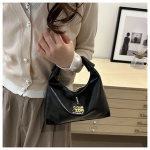 Close-up of black patent leather crescent hobo bag with a knotted handle and yellow text