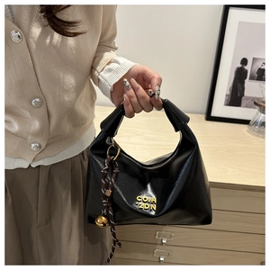 Detail of black semi-moon bag with gold logo and woven bell charm accessory