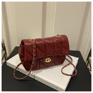 Détail du sac à chaîne en cuir matelassé bordeaux avec fermoir doré sur un livre