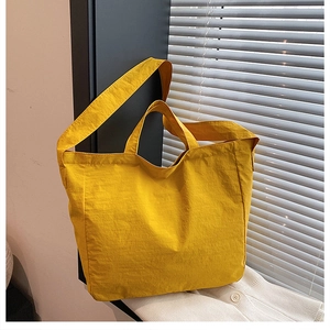 Detail of a ginger yellow nylon tote bag featuring durable handles and a crossbody strap