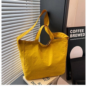 Close-up of bright yellow nylon tote bag with textured fabric detail and wide shoulder strap