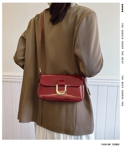 Detail of red patent leather shoulder bag with gold buckle on brown blazer outfit