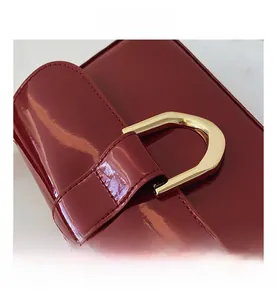 Detail of burgundy patent leather handbag featuring a gold horseshoe metal buckle
