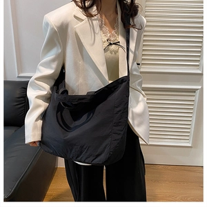 Close-up of minimalist black nylon tote bag with wide strap worn as a shoulder bag