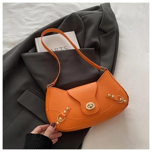 Macro detail of orange leather underarm bag with gold rivets and metallic twist lock
