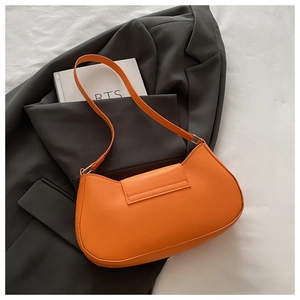 Detail shot of bright orange PU leather baguette bag on a grey blazer and book