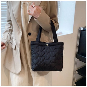Detail of black quilted tote bag featuring structured heart patterns and metal button closure