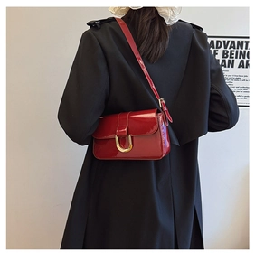 Macro shot of a red patent leather crossbody bag with a golden horseshoe buckle