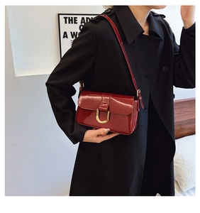 Detail of burgundy patent leather bag with gold horseshoe buckle on black trench coat