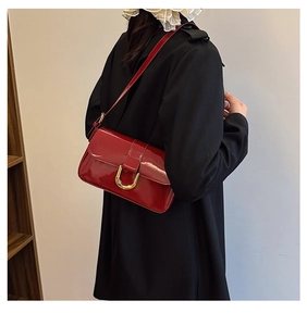 Close-up of a burgundy patent leather bag with a gold horseshoe buckle on a model shoulder