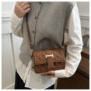 Detail einer braunen gesteppten Handtasche mit goldenem Metallverschluss und Schultergurt