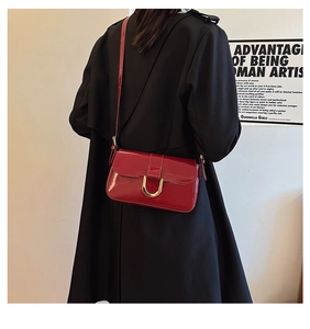 Detail of red patent leather crossbody bag with elegant gold U-shaped metal buckle clasp