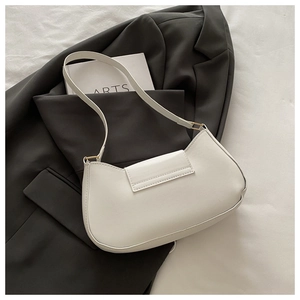 Minimalist white faux leather crescent shoulder bag on a grey blazer suit with art books