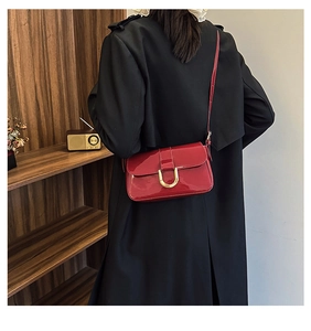 Detail of red patent leather shoulder bag with golden horseshoe buckle and glossy finish