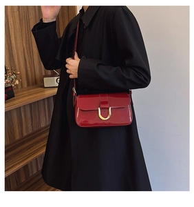 Detail of red patent leather shoulder bag with a gold horseshoe buckle on the front