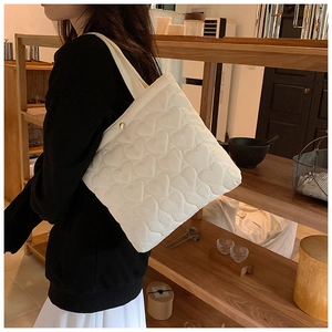 Detail of white quilted heart pattern tote bag worn by a model in a cafe setting